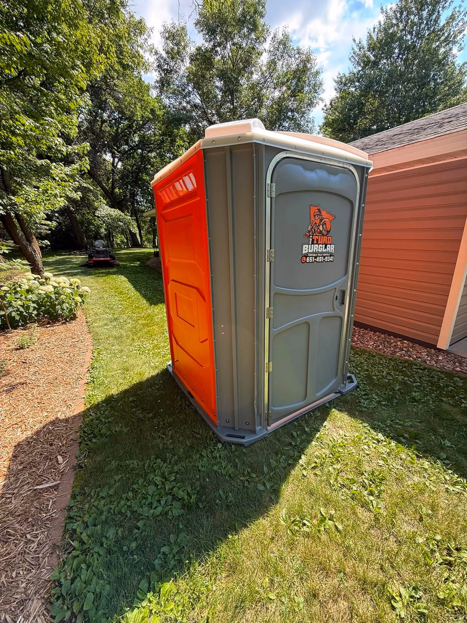 A wide handicapped accessible portable toilet with a ground level base on a mown lawn.