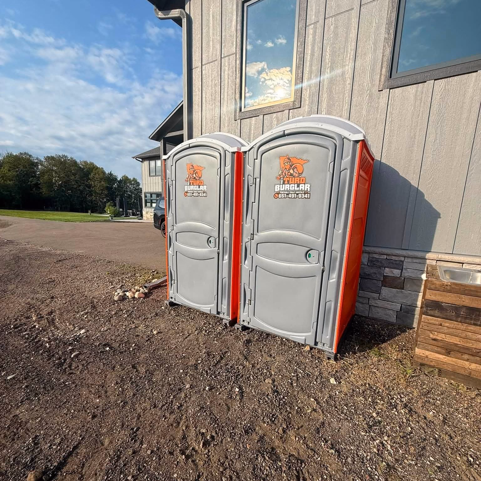Two portable toilets standing on bare ground beside a house under construction.