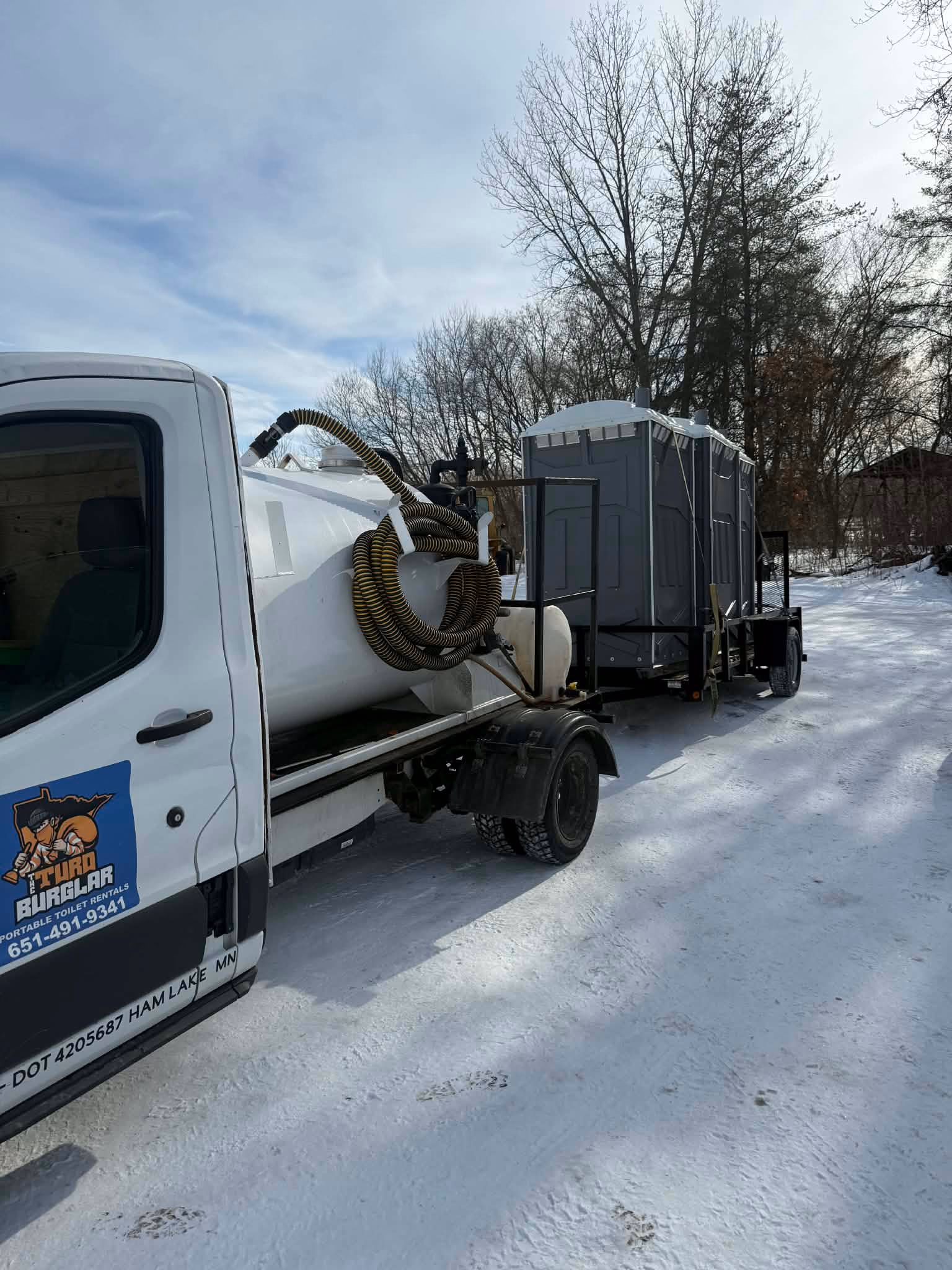 A white service truck with a pump tank working on a snow covered lot in winter.