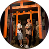 Two people posing under a bright orange torii gate at night.