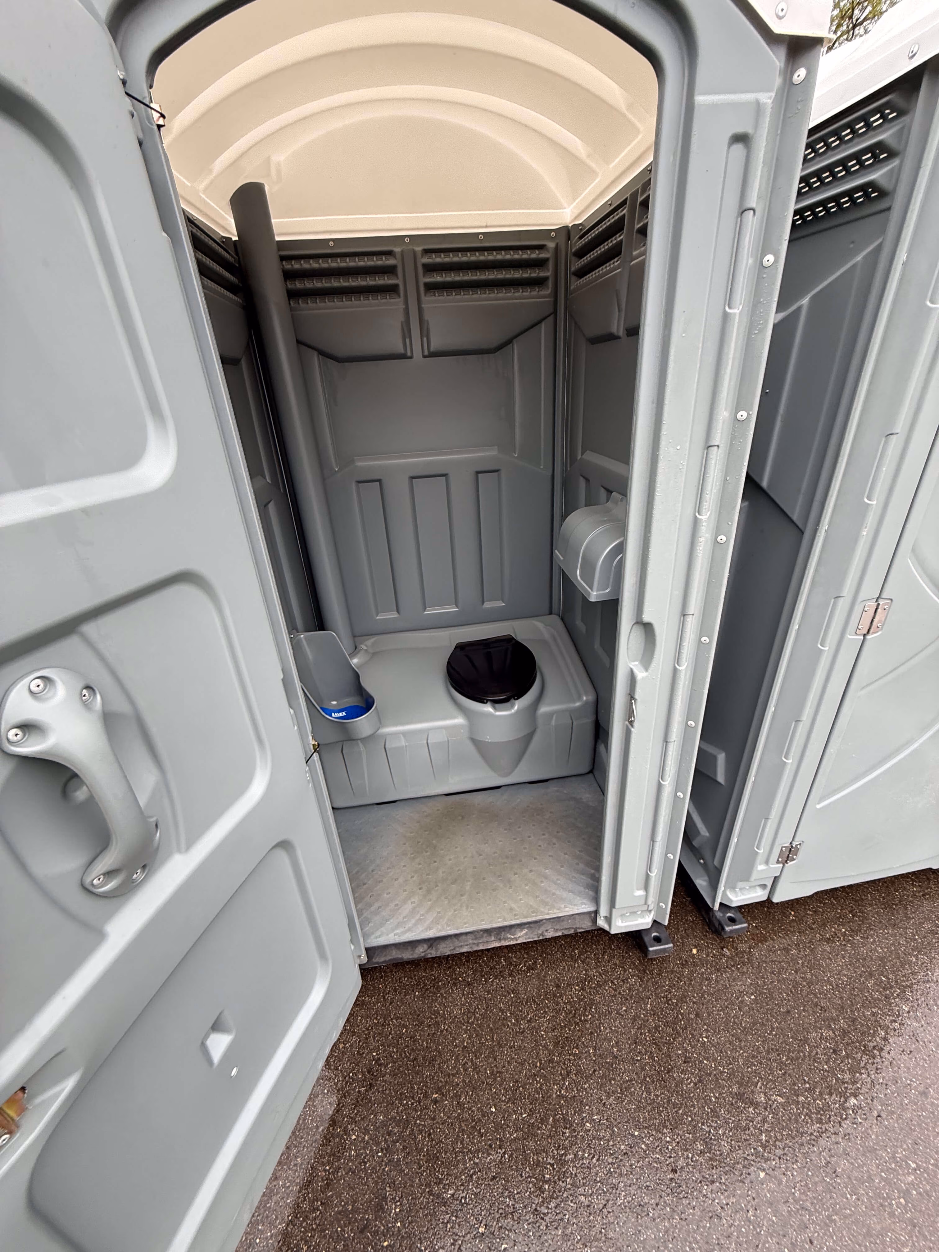 Interior of a gray portable toilet showing a plastic toilet seat, urinal, and toilet paper holder.